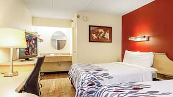 Una habitación de hotel con una cama, un escritorio con computadora, un espejo y un cuadro colgado en la pared.