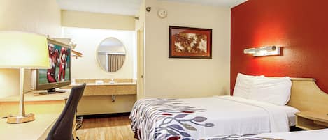 A hotel room with a bed, a desk with a computer, a mirror, and a wall-mounted picture.