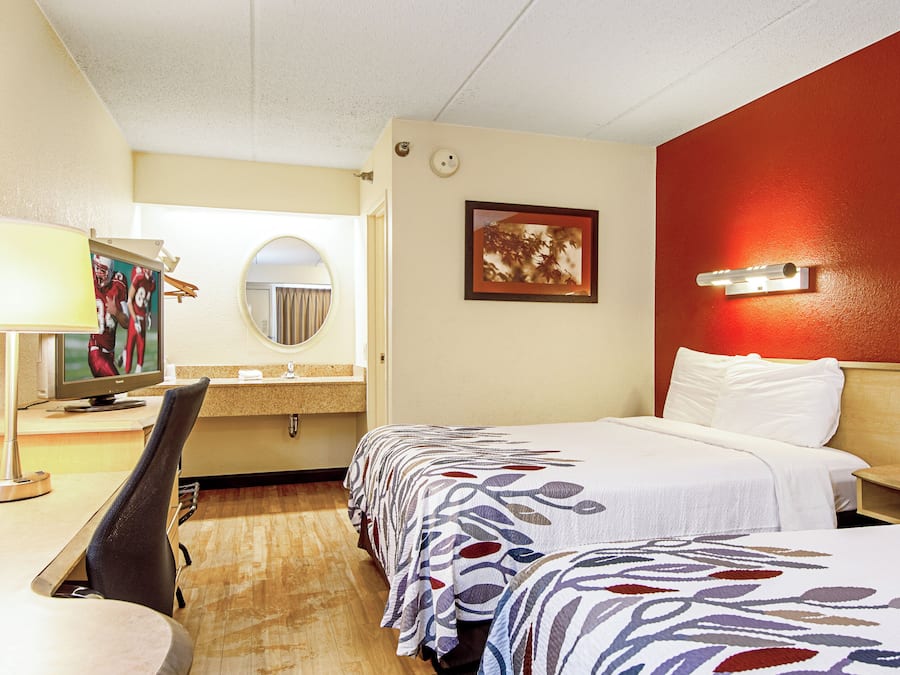 Quarto de hotel com cama, escrivaninha com computador, espelho e quadro na parede.