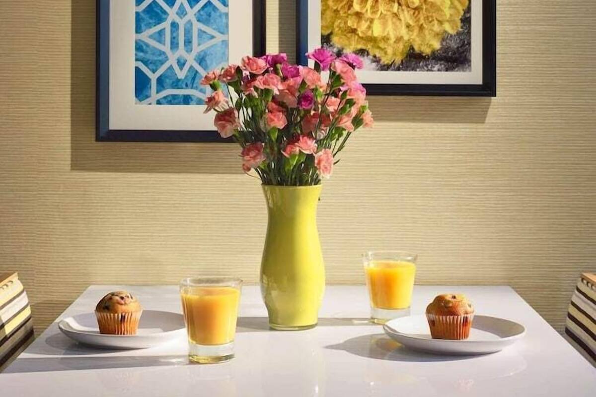 A table with a vase of flowers, two muffins, and two glasses of orange juice.