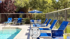 Zona de piscina con sillas reclinables azules y sombrillas, piscina con separadores de carril y un código QR en el suelo.