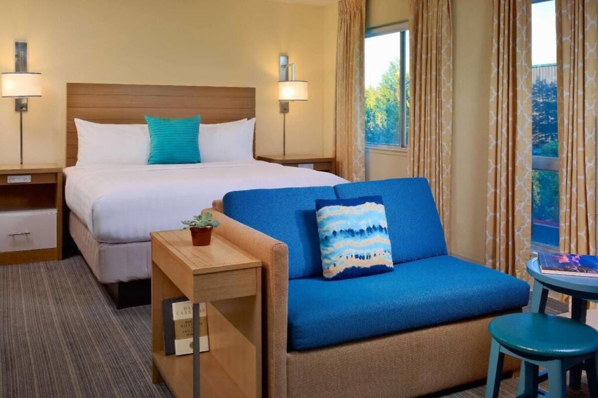 A hotel room with a bed, a sofa, a small table, and a window with curtains.