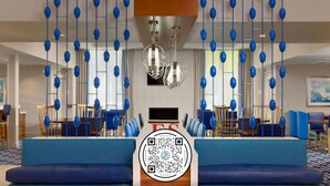 Un moderno vestíbulo de hotel con un espacio de estar central, una pantalla grande y un código QR sobre el sofá.
