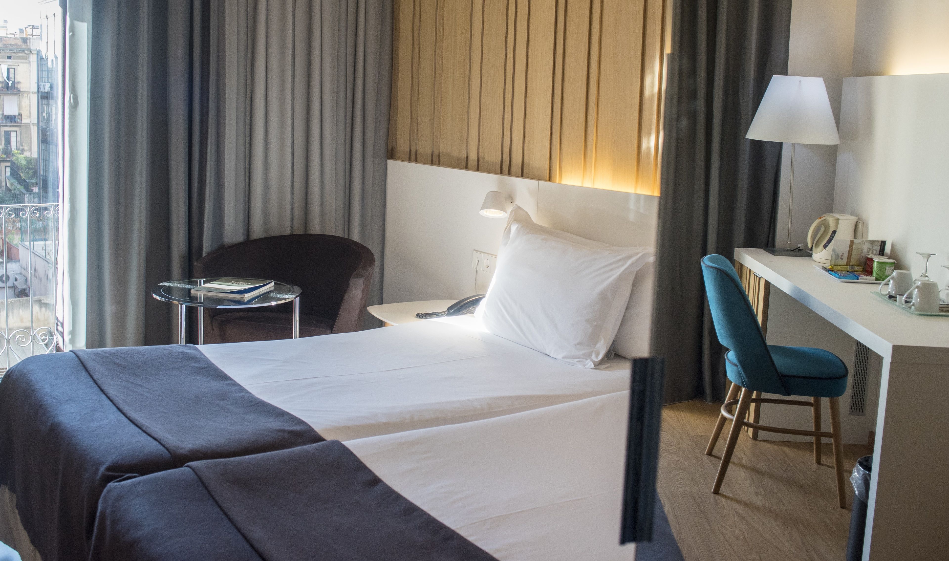 Een hotelkamer met een bed, een bureau, een stoel, een klein tafeltje en uitzicht op de stad.