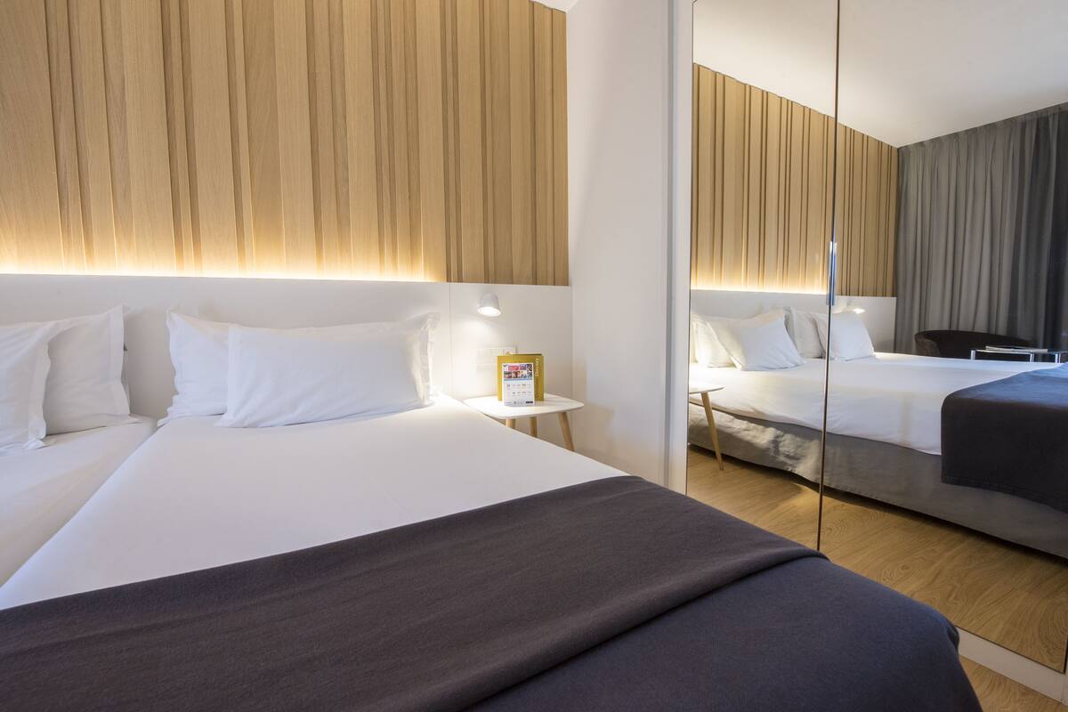 A hotel room with a large bed, a bedside table with a lamp, a mirror, and a wooden headboard.
