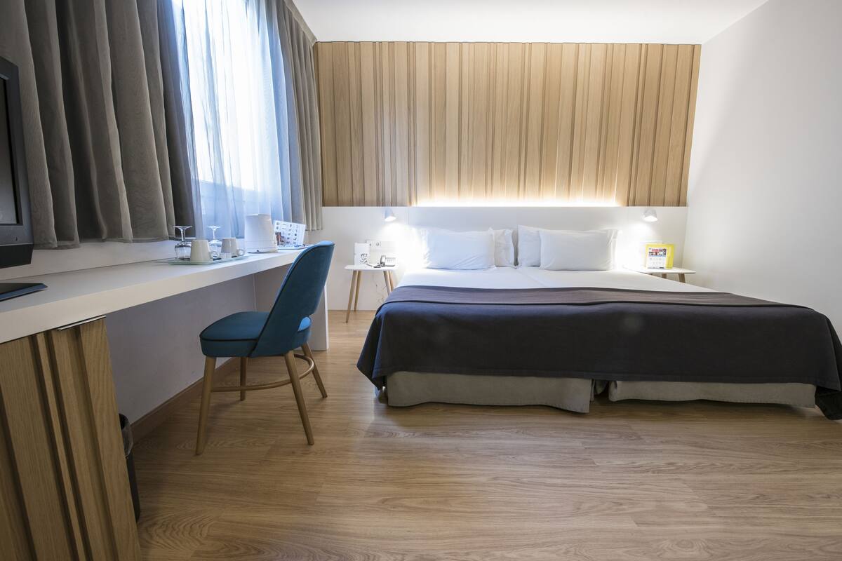 A hotel room with a bed, a desk, a chair, a TV, and a window with curtains.