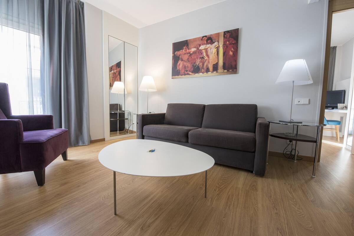 A modern living room with a grey sofa, a purple armchair, a white coffee table, and a painting on the wall.