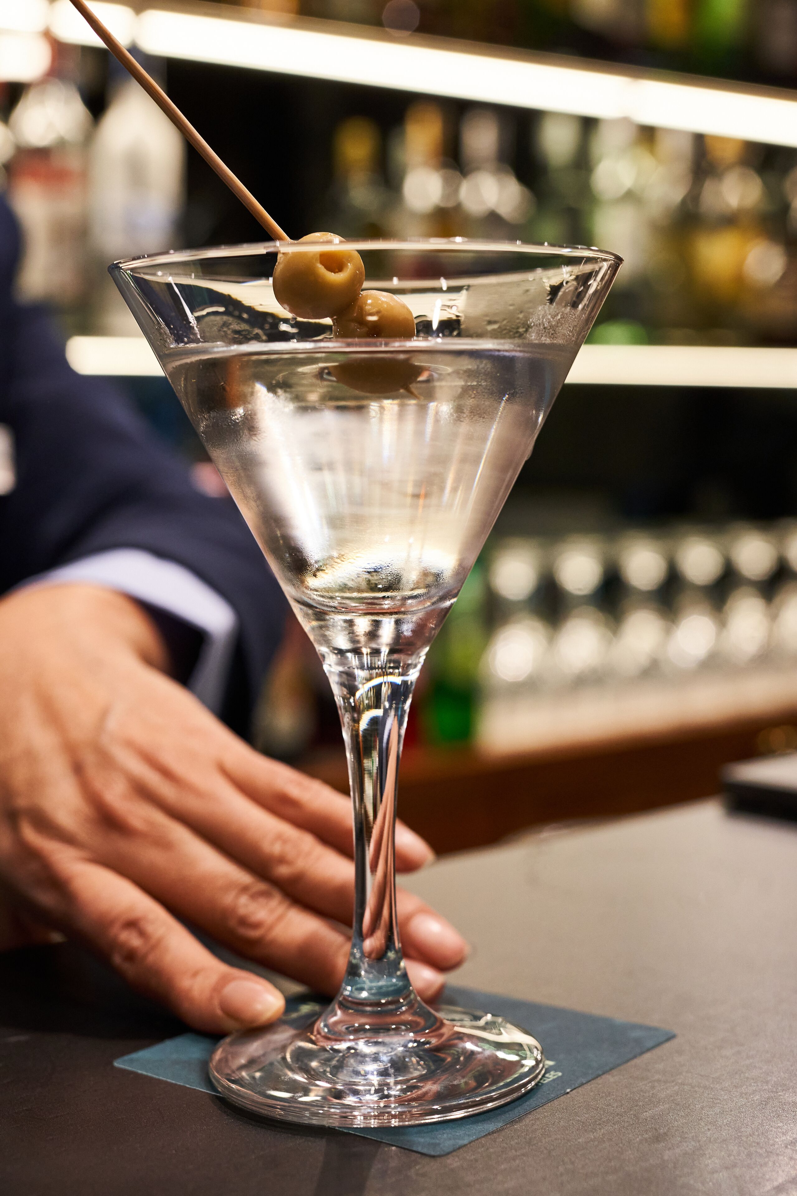 Un verre à martini avec une olive, posé sur le comptoir d’un bar.