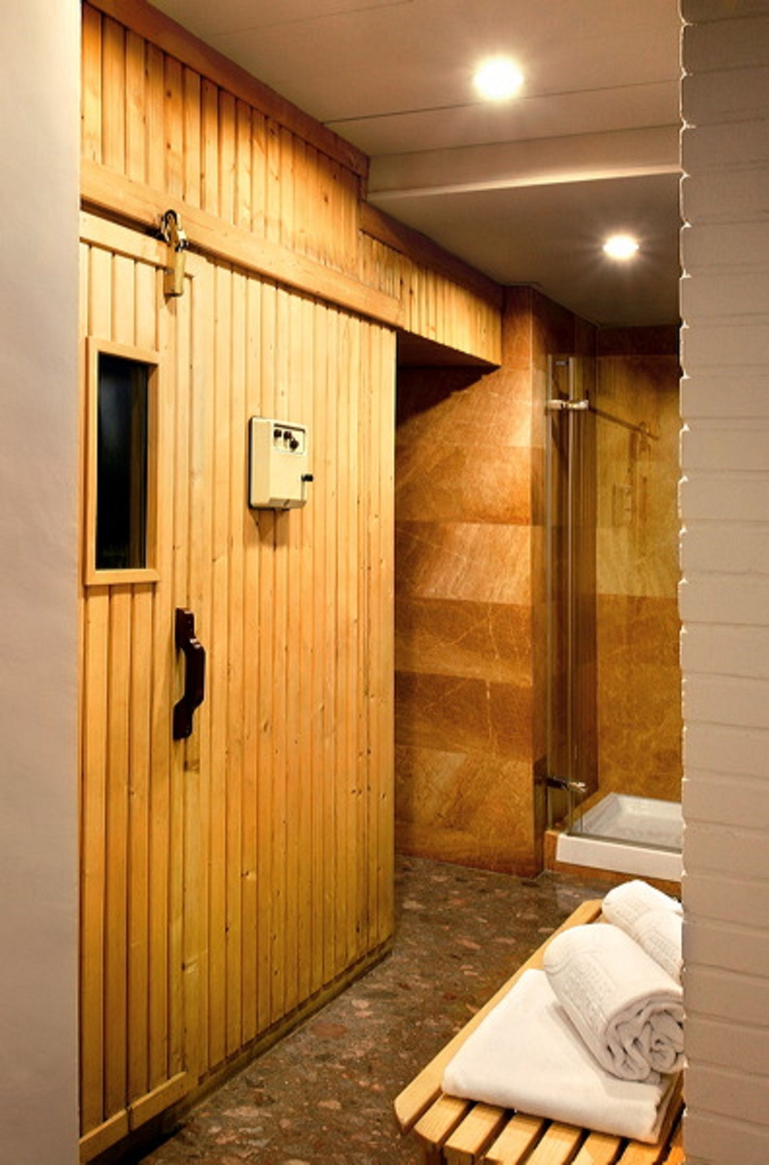A wooden-paneled room with a bench, a towel rack, and a shower area.