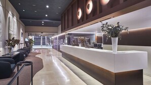 A modern reception area with a long counter, seating area, and a large potted plant. - Hotel Silken Ramblas (Barcelona)