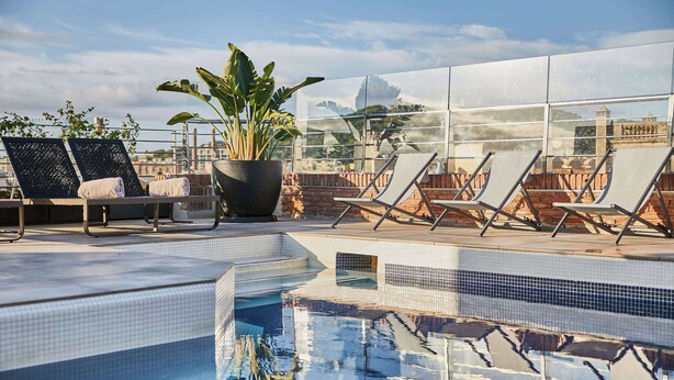 A rooftop pool area with lounge chairs, a potted plant, and a clear view of the cityscape. - Hotel Silken Ramblas (Barcelona)