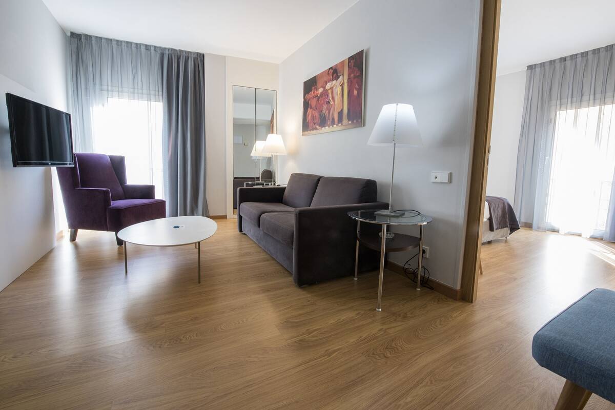 A modern living room with a sofa, armchair, round coffee table, and a TV mounted on the wall.