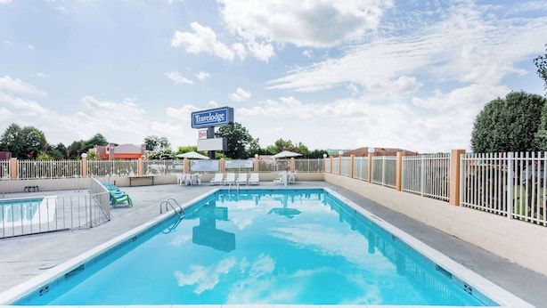 Una piscina rectangular con valla blanca alrededor, un cartel que indica 'Travelodge', y un cielo despejado con nubes.