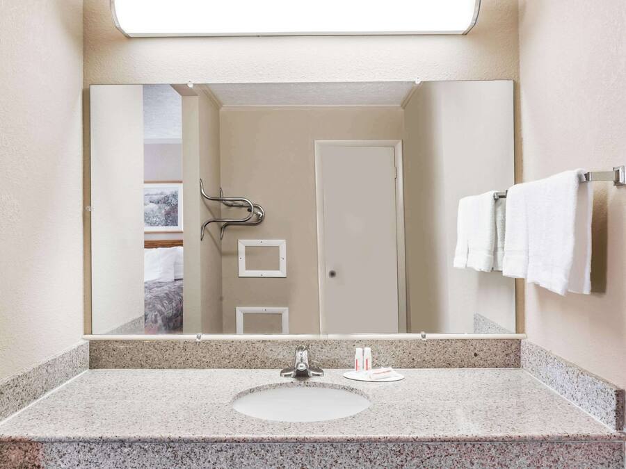 A bathroom with a granite countertop sink, a mirror, and a towel rack with white towels.