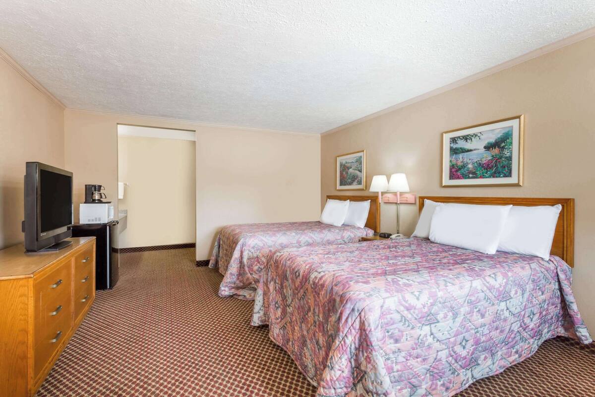 A hotel room with two beds, a television, a coffee maker, and artwork on the walls.