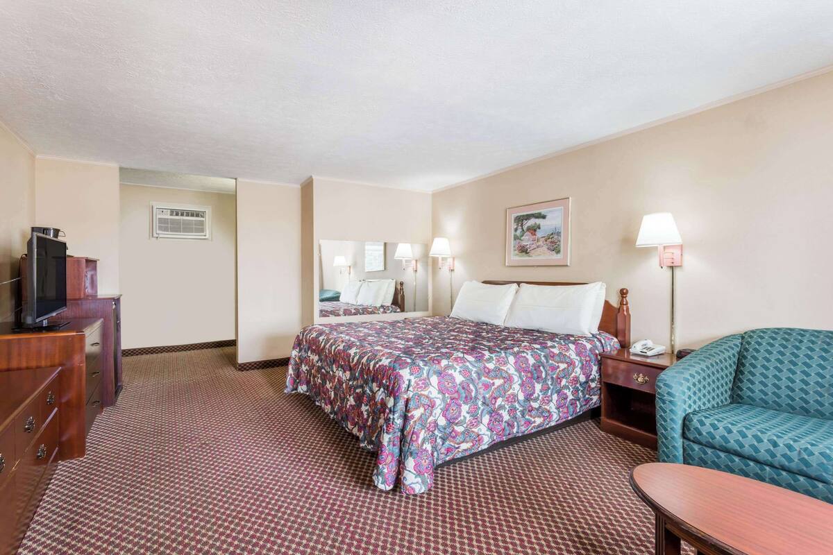 A hotel room with a bed, a desk, a chair, a TV, and a lamp.