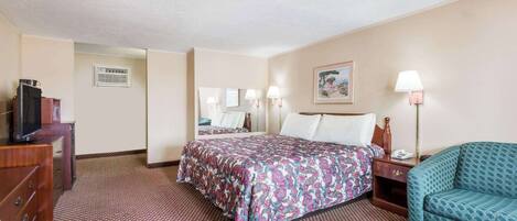 A hotel room with a bed, a desk, a chair, a TV, and a lamp.