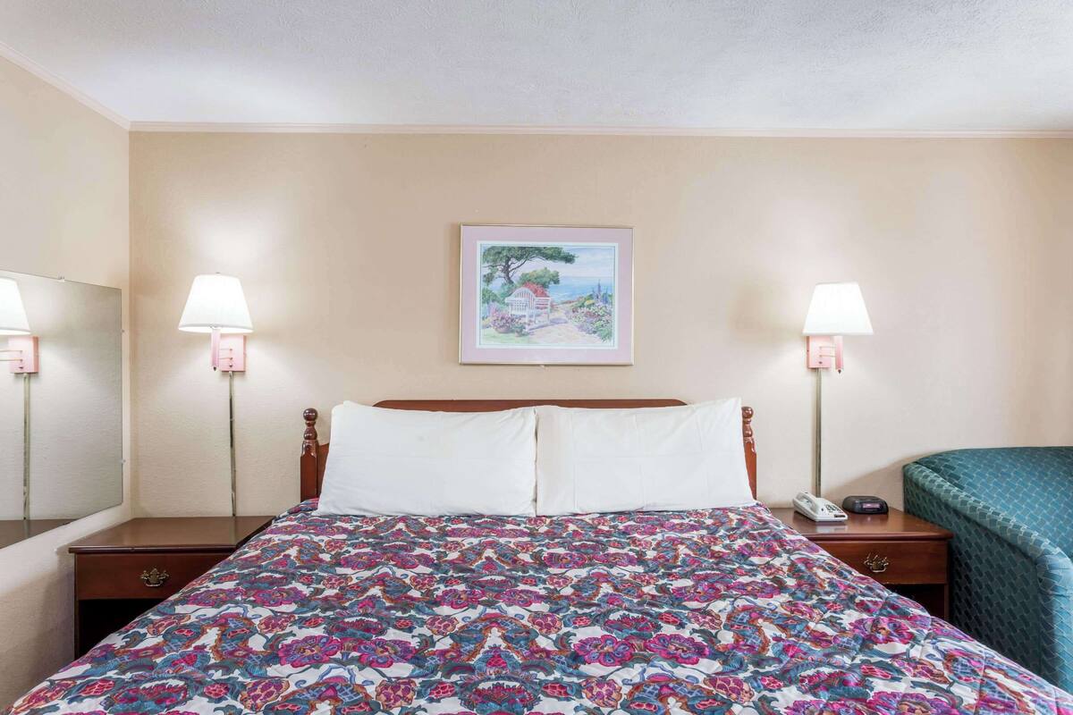A hotel room with a large bed, two bedside lamps, a nightstand with a phone, and a framed picture on the wall.