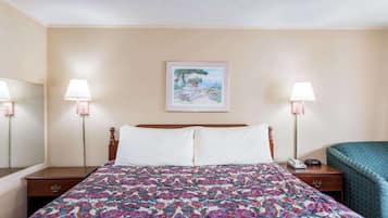 A hotel room with a large bed, two bedside lamps, a nightstand with a phone, and a framed picture on the wall.