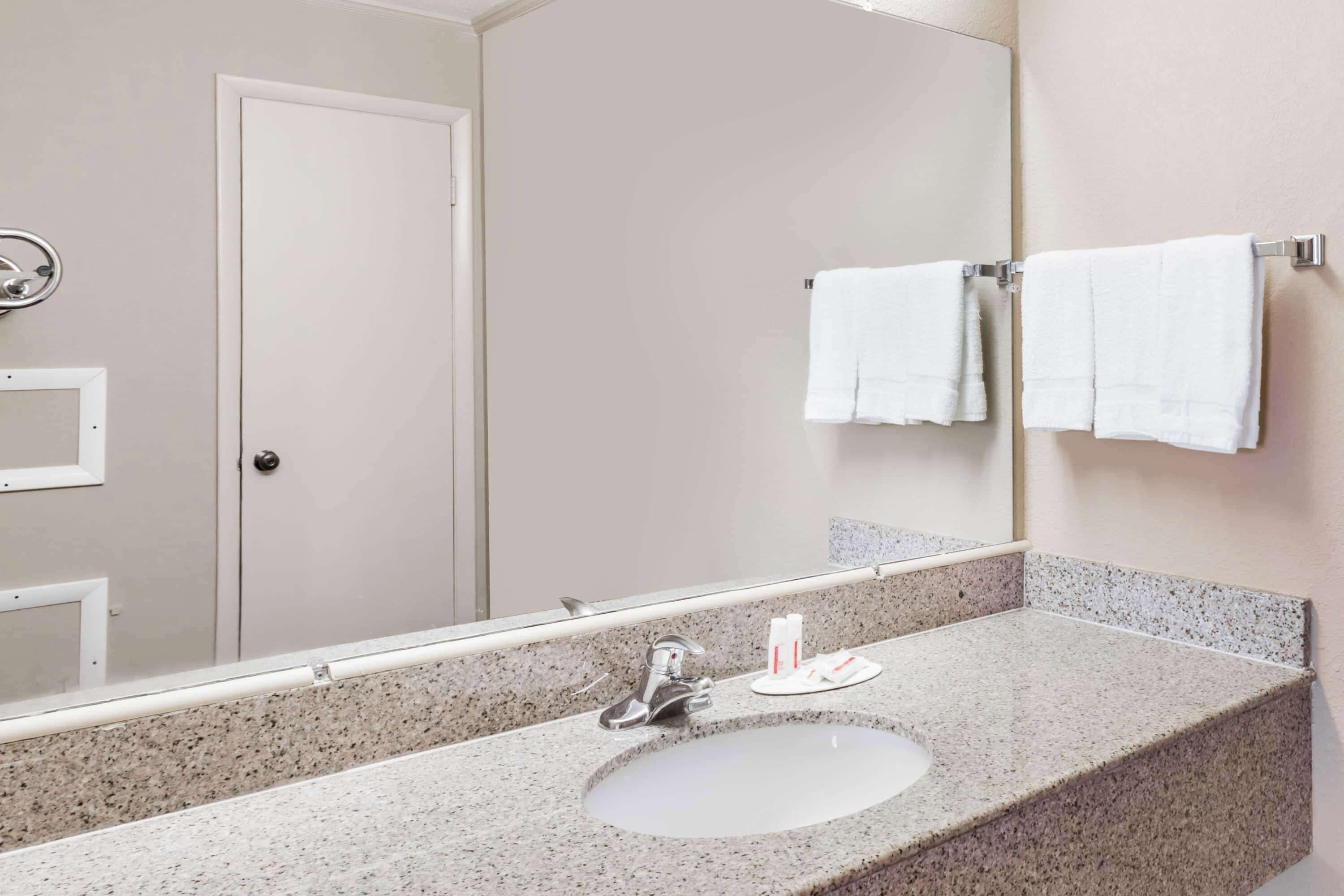 A bathroom with a granite countertop sink, a mirror, and two white towels hanging on a towel rack.