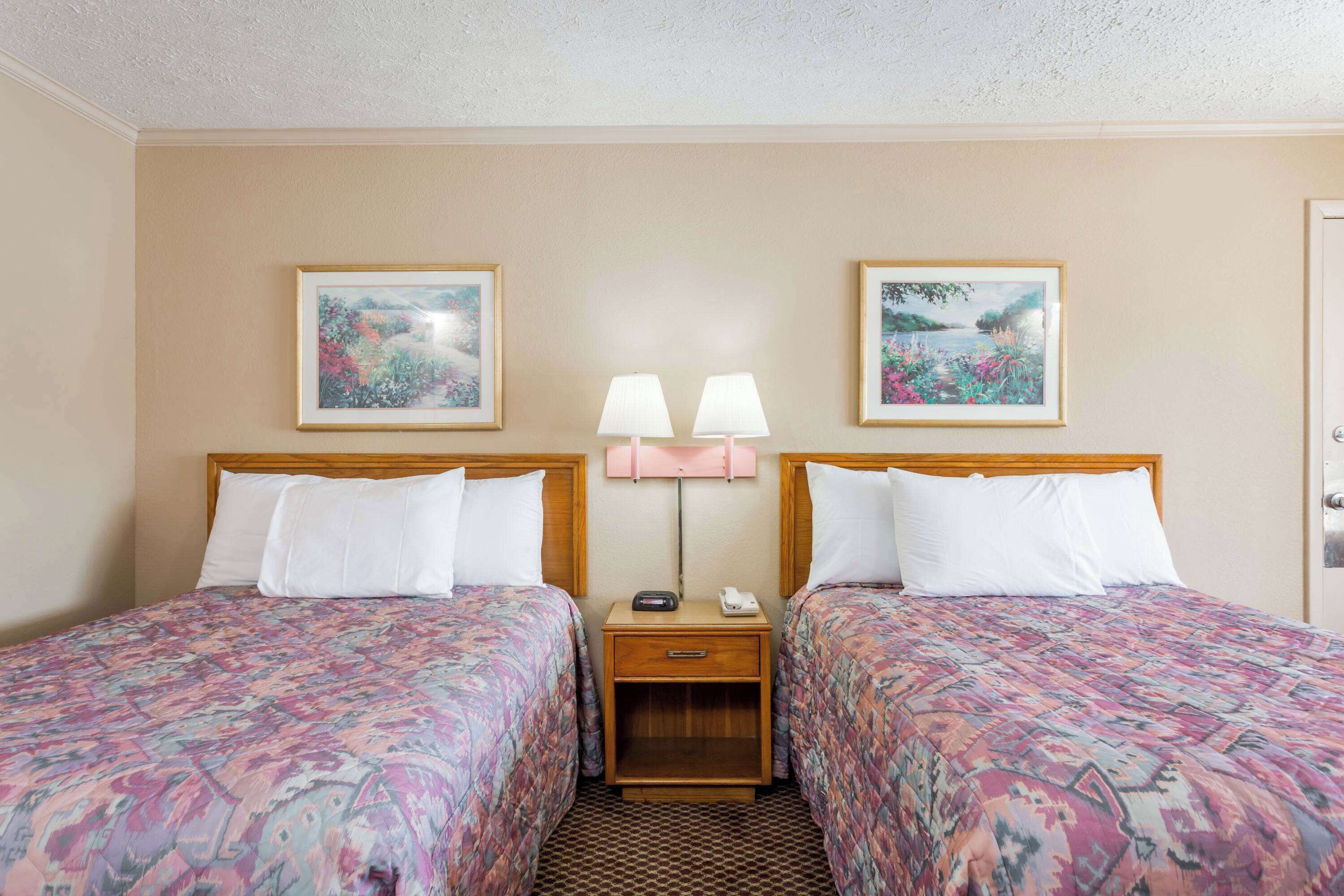 A hotel room with two beds, a nightstand with lamps, and framed pictures on the wall.