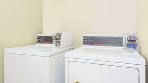 Dos secadoras comerciales blancas una al lado de la otra en un cuarto de lavandería con paredes color crema.