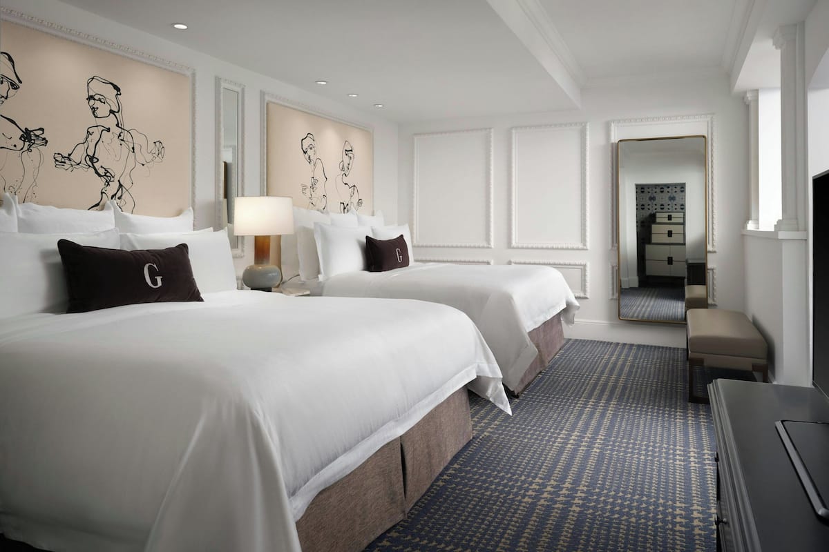 A hotel room with two beds, a desk, a lamp, and a patterned carpet.