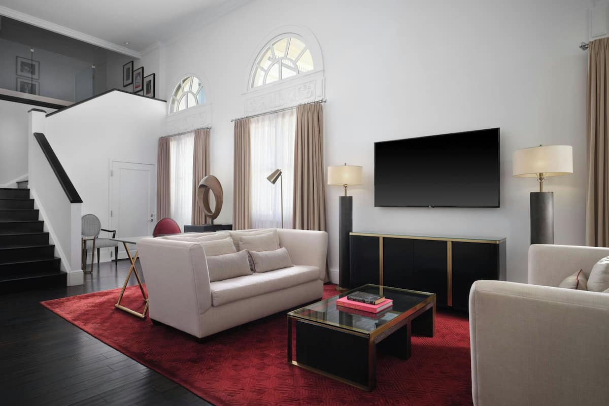 A modern living room with a staircase, a flat-screen TV, and a red rug.