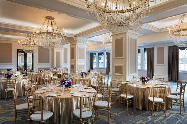 Un comedor formal con mesas redondas, sillas doradas y candelabros.