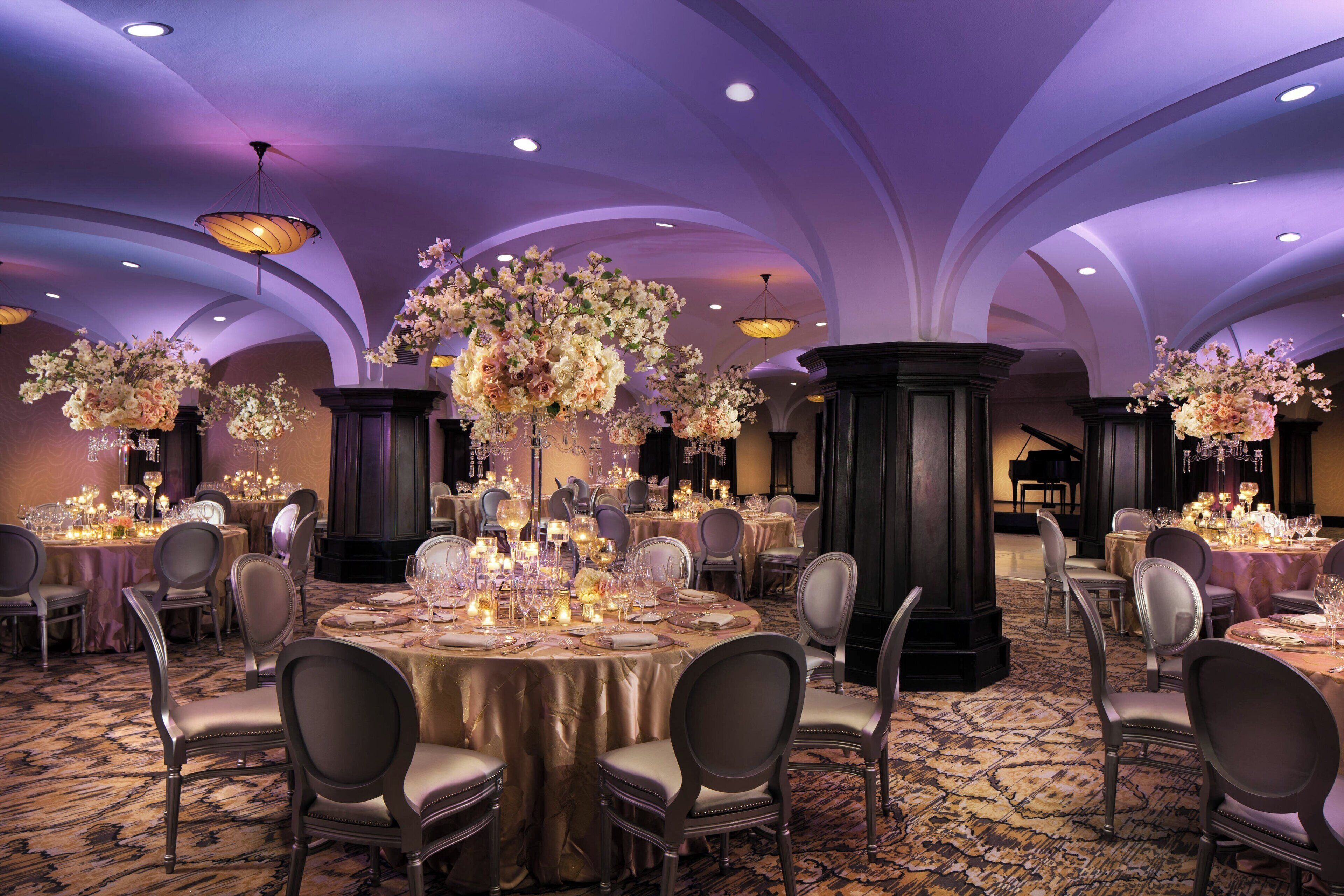 A banquet hall with round tables, chairs, and floral centerpieces.