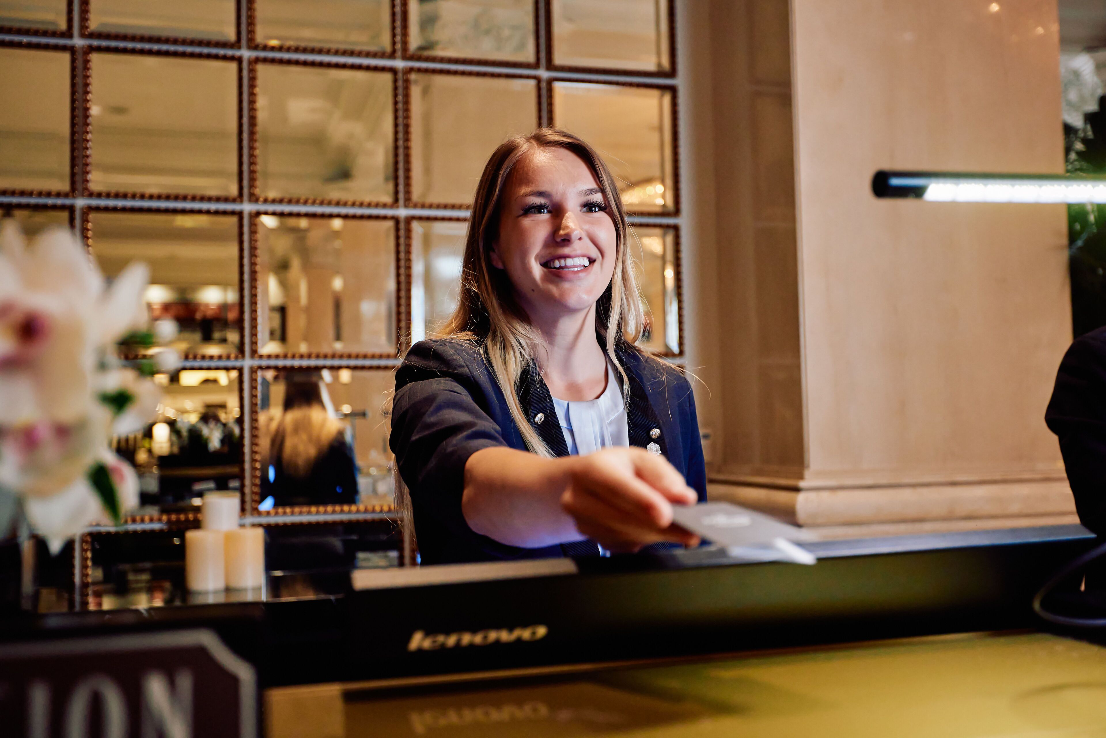 Una persona en la recepción con un computador Lenovo, un espejo y una flor al frente.
