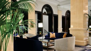 A lobby with a blue sofa, a white armchair, and a glass coffee table. There are large columns and a staircase in the background. - The US Grant, a Luxury Collection Hotel, San Diego (San Diego)
