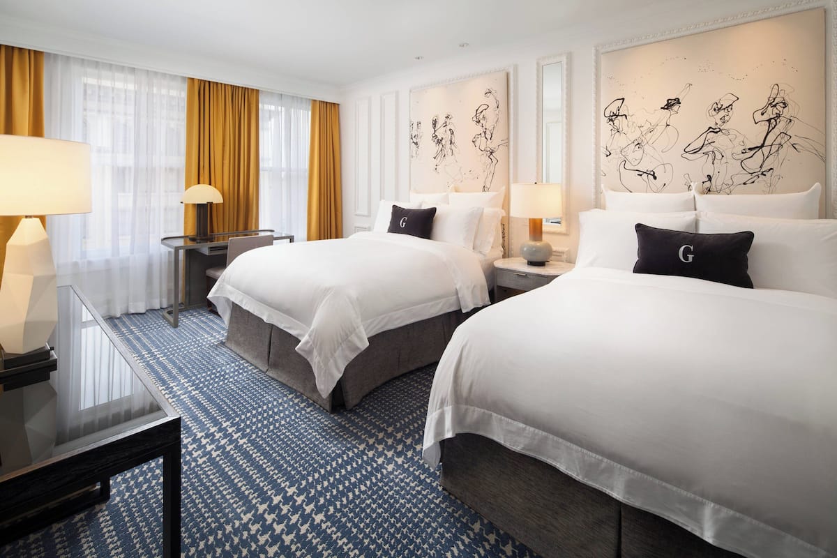 A hotel room with two beds, a desk, and a large window with curtains.
