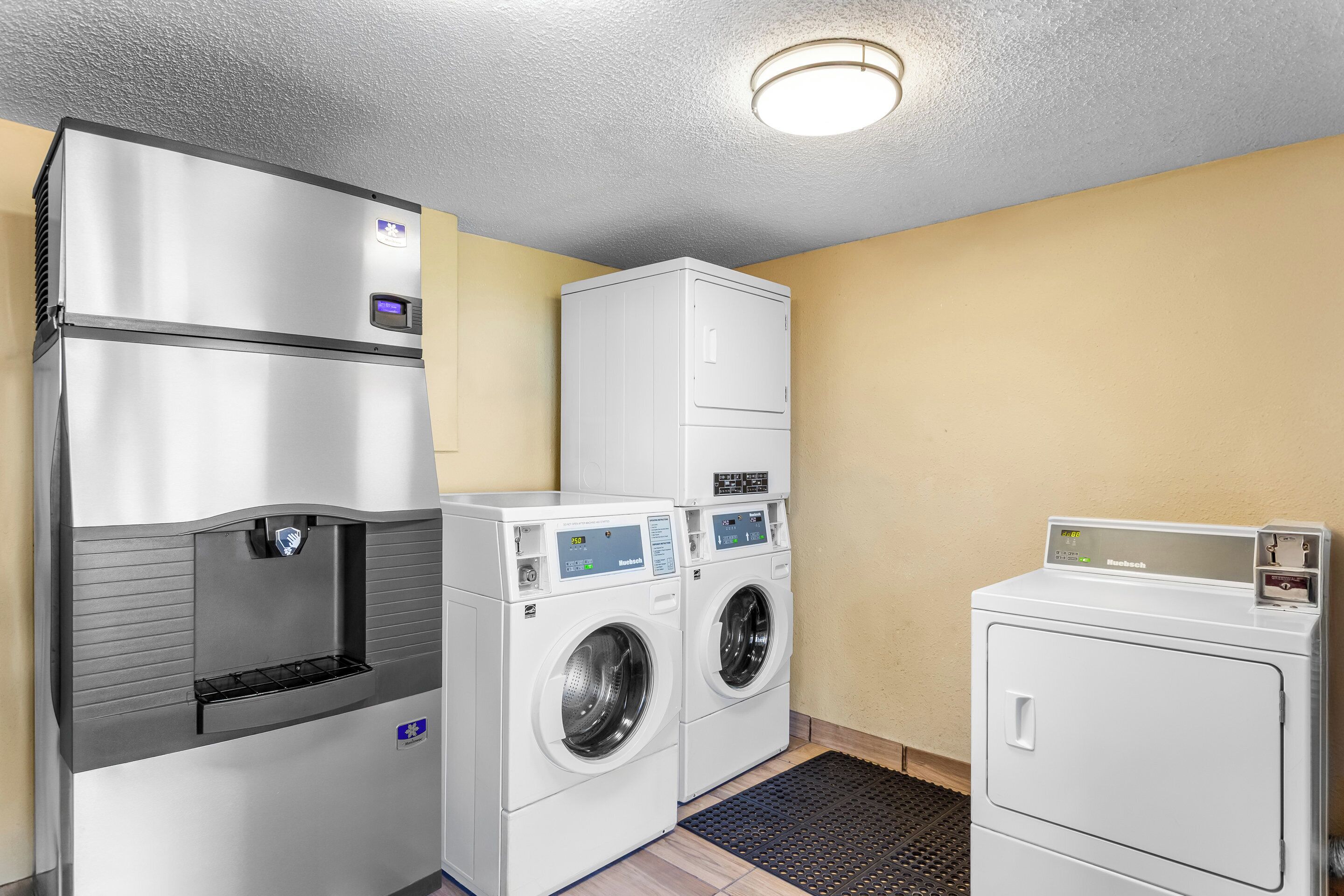 A laundry room with a stainless steel refrigerator, two front-loading washers, and a stacked dryer.