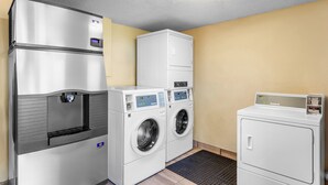 A laundry room with a stainless steel refrigerator, two front-loading washers, and a stacked dryer. - Red Roof Inn PLUS+ Chicago - Hoffman Estates (Hoffman Estates)