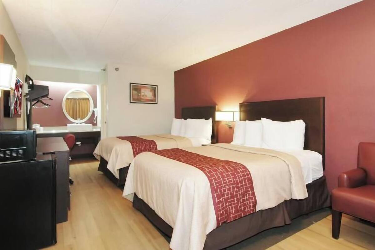 Ein Hotelzimmer mit zwei Betten, einem Schreibtisch, einem Stuhl, einem Fernseher und einem Spiegel.