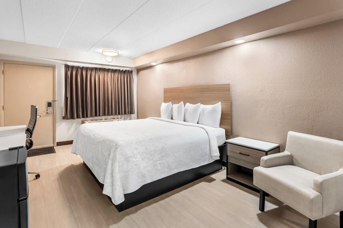 A modern hotel room with a large bed, a bedside table, a chair, and a desk.