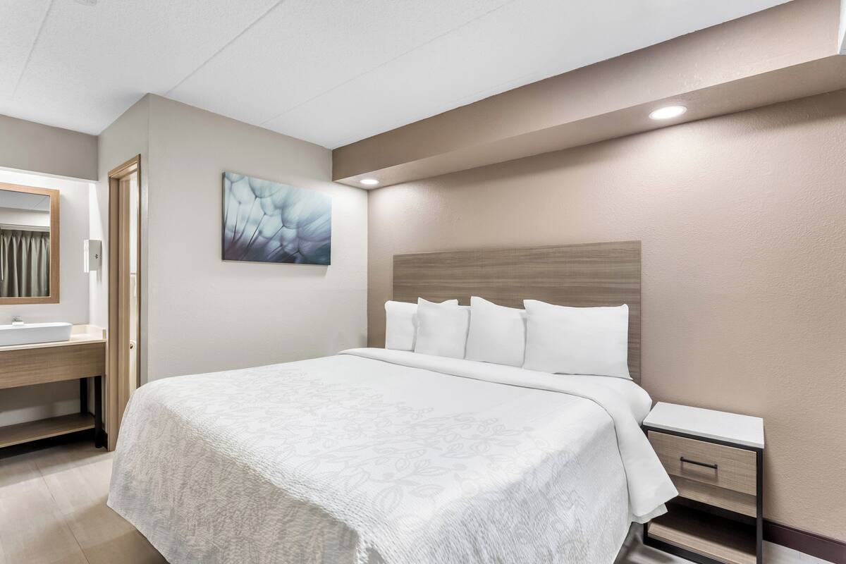 Ein Hotelzimmer mit einem großen Bett, einem Nachttisch, einem Waschtisch und einem Badezimmer mit Waschbecken und Spiegel.