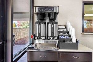 A coffee machine with a digital display, a coffee dispenser, and a coffee maker. There are cups and a coffee pod holder on the counter.