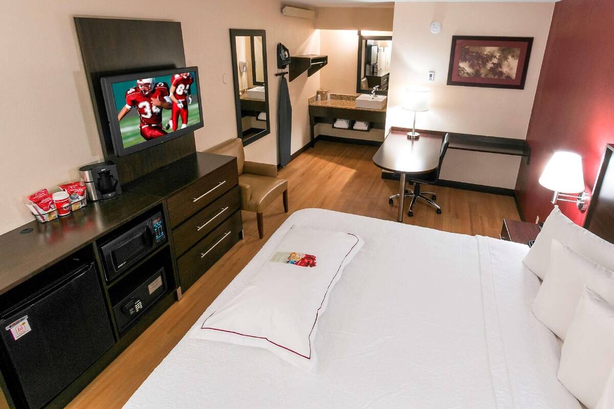 Ein Hotelzimmer mit Bett, Schreibtisch, Stuhl, Fernseher, Kaffeemaschine und Spiegel.