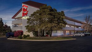 A Red Roof Plus hotel with a modern design, featuring a large tree in front and a parking lot with several cars. - Red Roof Inn PLUS+ Chicago - Hoffman Estates (Hoffman Estates)