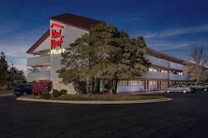 A Red Roof Plus hotel with a modern design, featuring a large tree in front and a parking lot with several cars. - Red Roof Inn PLUS+ Chicago - Hoffman Estates (Hoffman Estates)