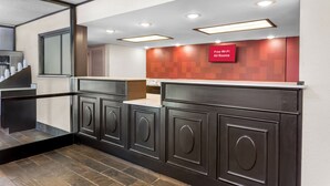 A modern hotel lobby with dark wood cabinetry, a red accent wall, and a sign indicating free Wi-Fi in all rooms. - Red Roof Inn PLUS+ Chicago - Hoffman Estates (Hoffman Estates)