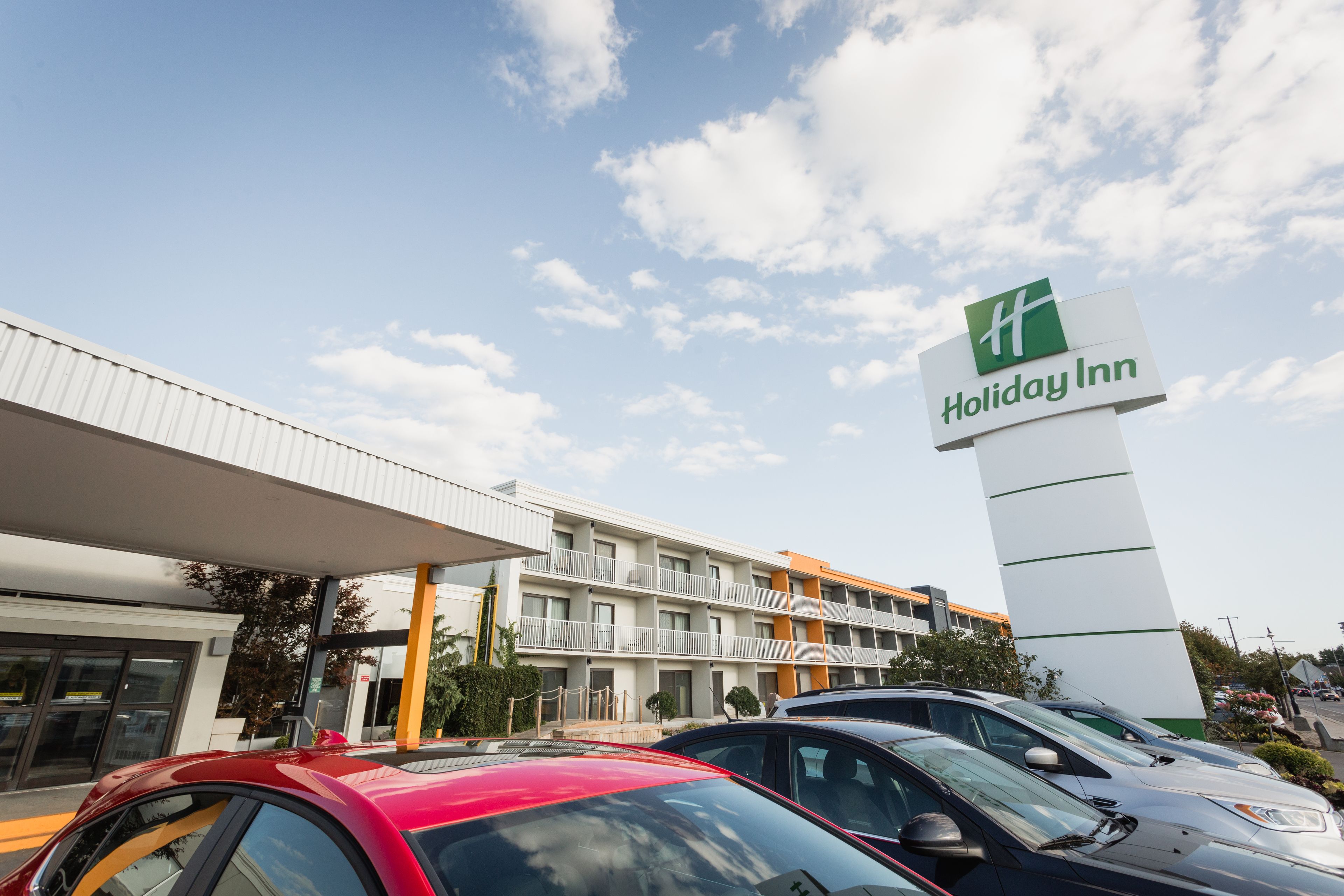 A Holiday Inn hotel with a multi-story building, a covered parking area, and several cars parked in front.