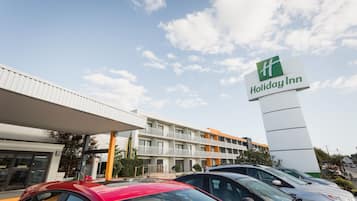 A Holiday Inn hotel with a multi-story building, a covered parking area, and several cars parked in front.