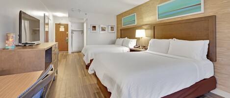 A hotel room with two beds, a desk, a mirror, and a bathroom door.