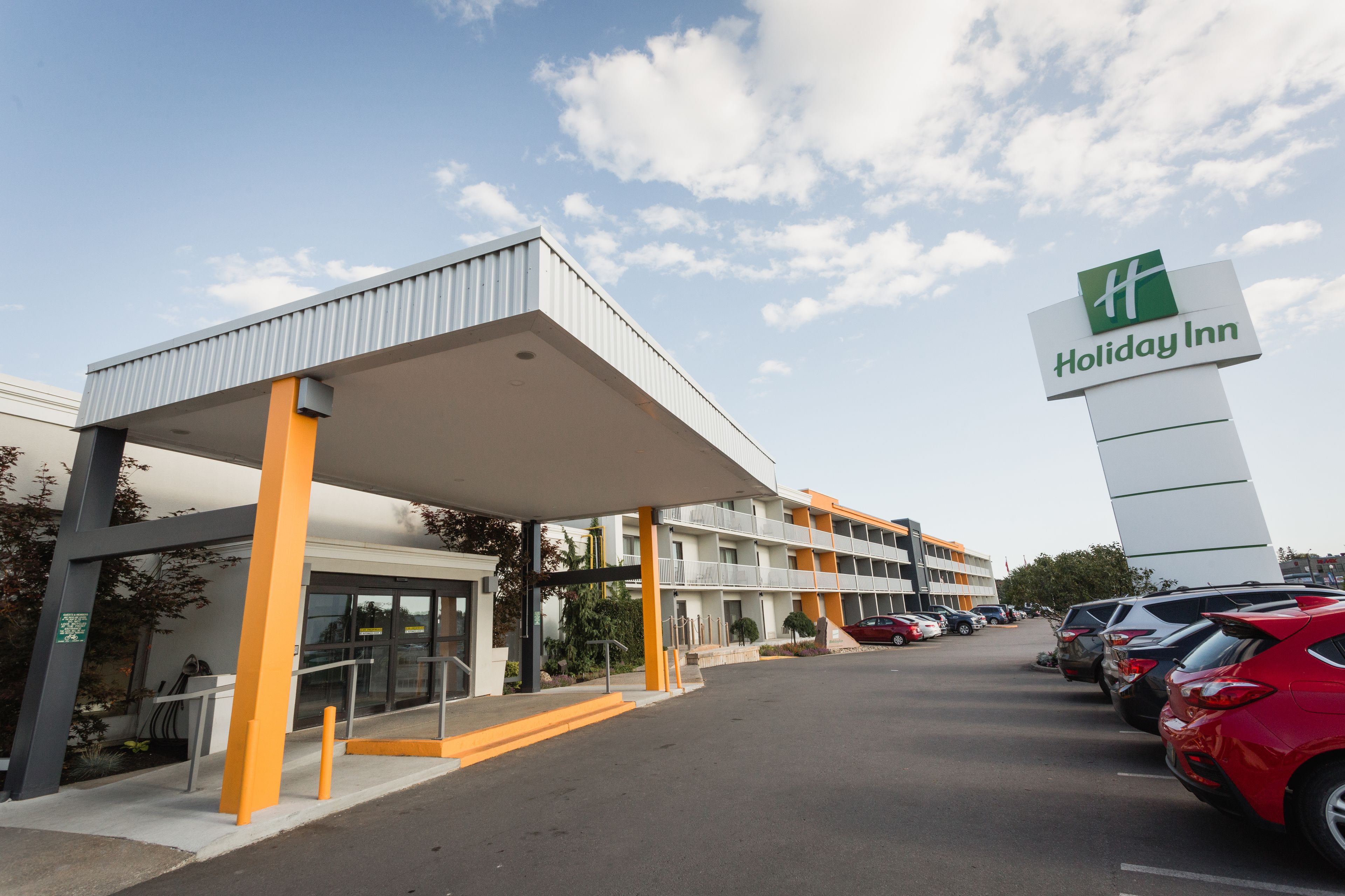 A Holiday Inn hotel with a covered entrance, a parking lot with several cars, and a clear sky.