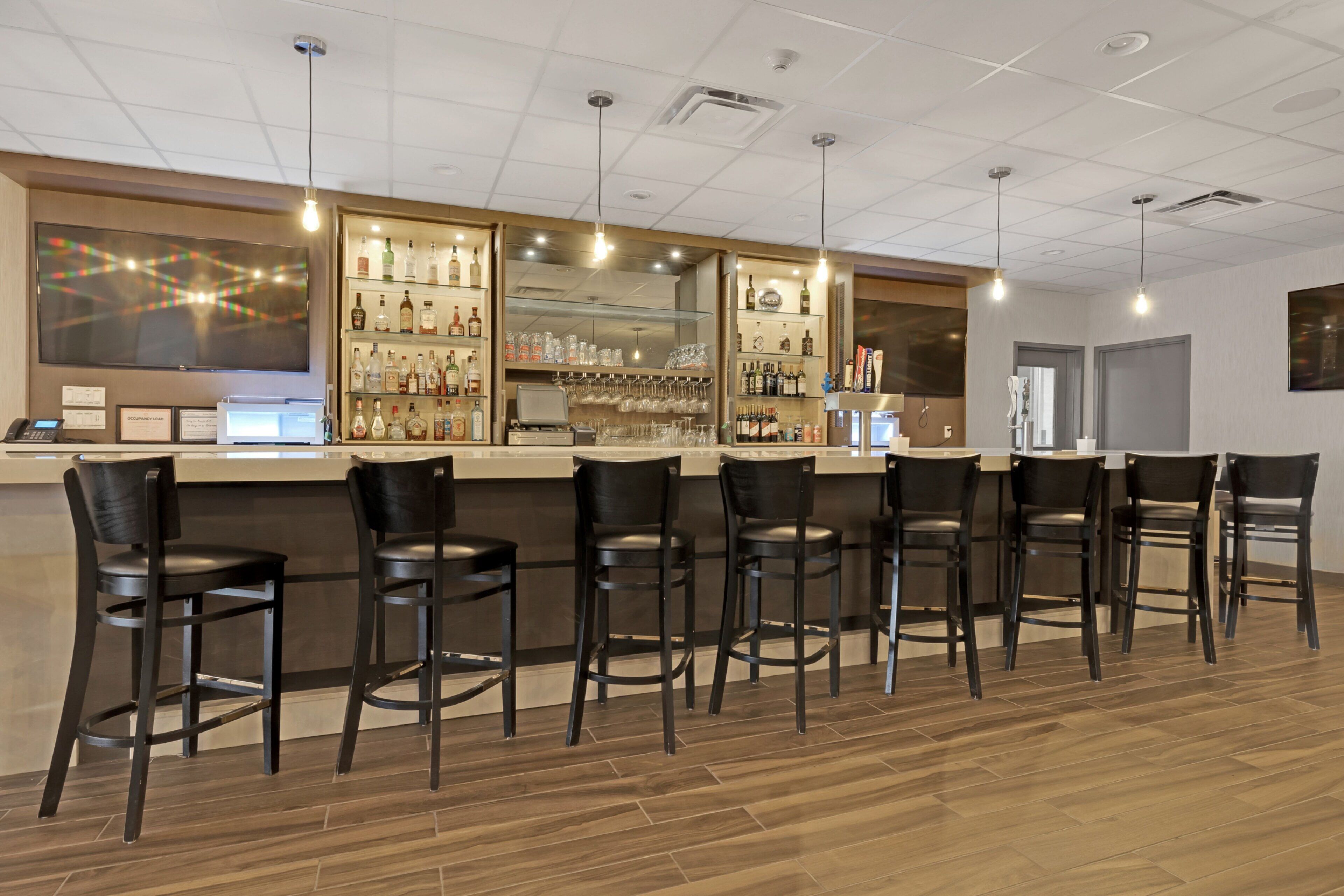 A bar area with a counter, bar stools, and shelves of bottles and glasses.