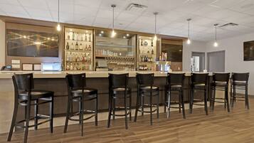 A bar area with a counter, bar stools, and shelves of bottles and glasses.