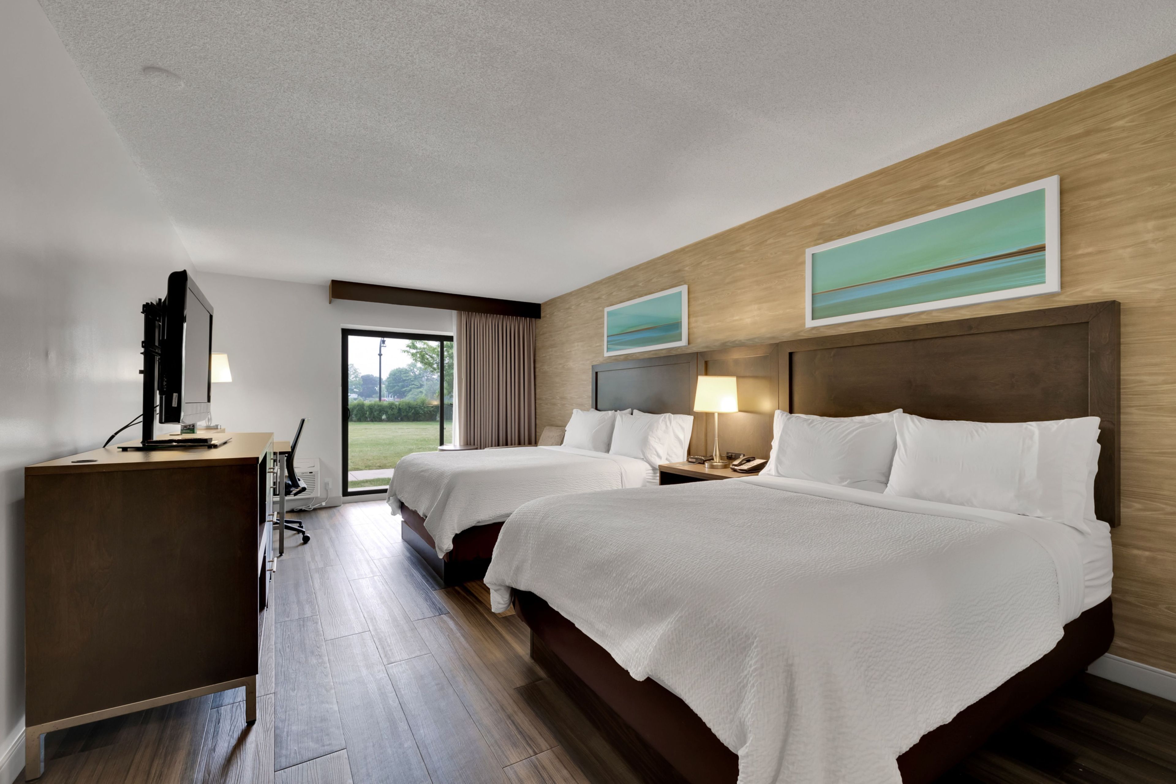 Een hotelkamer met twee bedden, een bureau met een computer en uitzicht op de omgeving.